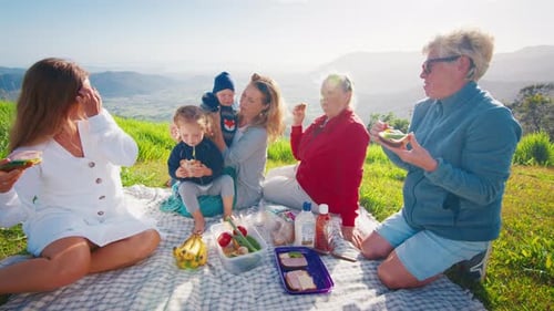 Big Family Have Picnic on the Green Hill in the Mountains at Sunrise