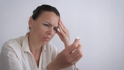 Woman Holding Pill with Hand on Forehead Indoors