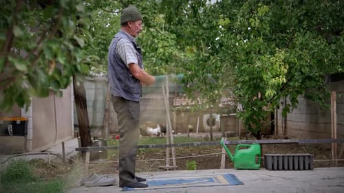 Muslimischer älterer Mann betet in seinem Garten mit Hühnern im Hintergrund