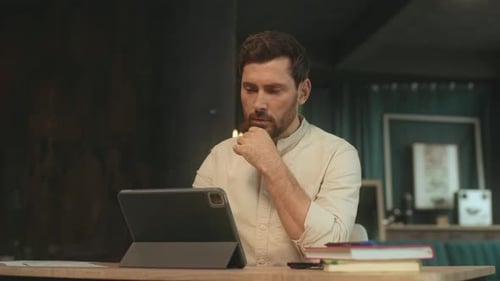 Attractive Bearded Man Sitting at Desk Use Tablet Computer Work Hold Pen in Office Thinking Camera