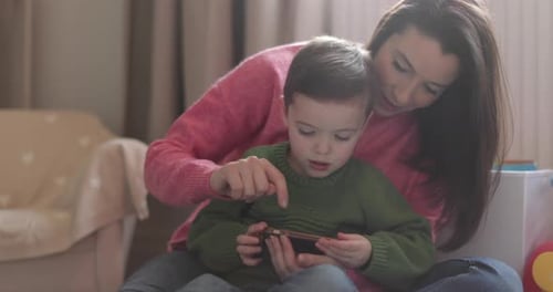 Caring Woman Watching Young Boy Play on Phone