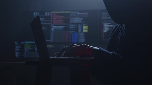 Hooded Hacker Typing on Laptop in Dark Room