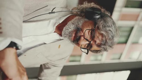 Mature businessman and headphones, sits in an outdoor cafe and works using tablet
