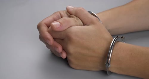 Handcuffed Hands Clasped Together on Gray Table