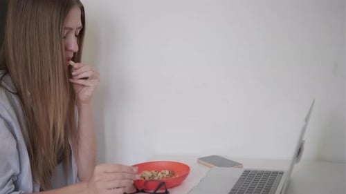 Young Woman Eating Nuts While Working on Laptop at Home Healthy Snack Concept