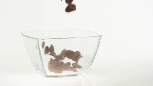 Fresh healthy food. Chocolate cereal flakes fall in a transparent square bowl on a white background