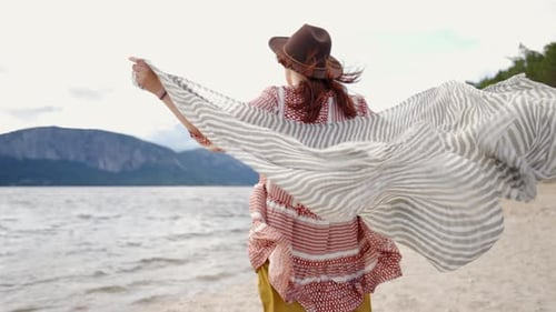 Woman Holds Flowing Scarf on Sandy Lake Beach