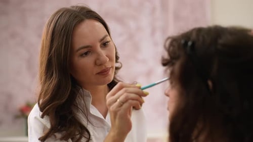 Closeup Rear View of Working Professional Makeup Artist Applying Eyeshadow to Eyelids of Young