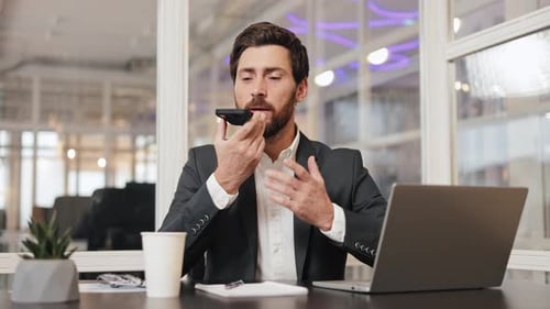 Businessman in Suit Working on Laptop and Talking on Phone at Office Desk