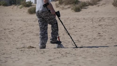 Man with a Metal Detector Walks Along a Sandy Beach on the Seashore Slow Motion