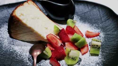 A slice of cheesecake served with fresh strawberries and kiwi, garnished with powdered sugar on a pl