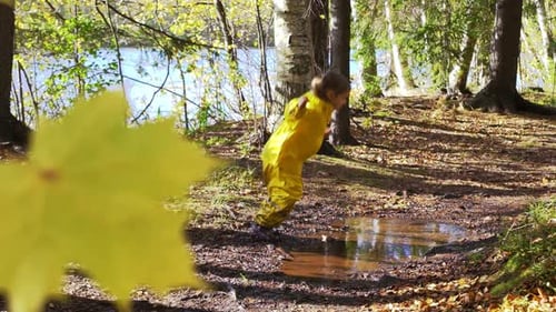 Happy Child in Yellow Rain Suit Jumping in Puddle on a Sunny Day