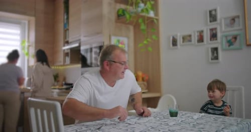 Father sitting at dining table interacting with young son, family moment in cozy kitchen, casual