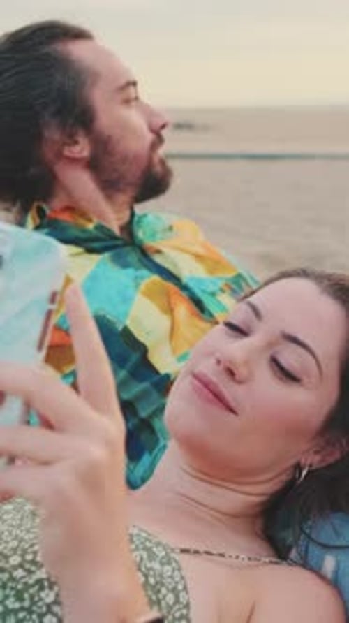 Close up, young couple relaxing on the beach. Young woman using mobile phone