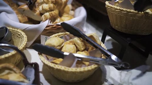 Assorted sweet and savory pastries in wicker baskets with tongs for serving at an event buffet.