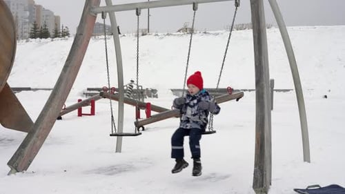 Young Boy Swinging at Snowy Playground