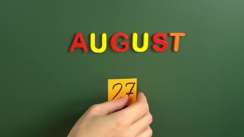 Hand sticking a sticker 27 August calendar day on school board. 27 date of august. Twenty seventh