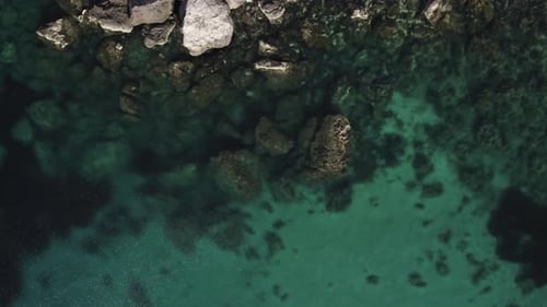 AERIAL - Turquoise waters give way to rocky cliffs at a beach, top down view