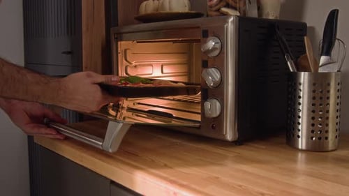 Man Putting Pizza into Toaster Oven in Kitchen