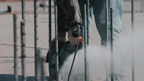 Worker Cutting Steel Rebar with Angle Grinder Between Rods Close Up