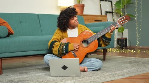 Woman Plays Guitar at Home Using Laptop