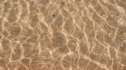 Sunlit Water Rippling on Sandy Beach