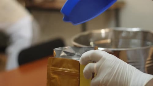 Gloved Hands Scooping Coffee Beans into Bag