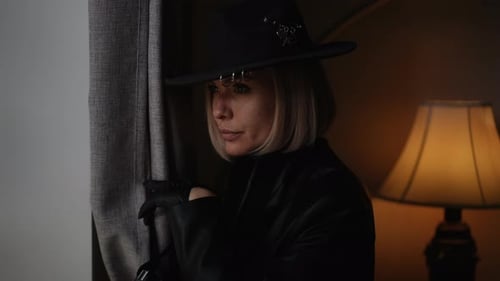 Woman with camera looks through opening in curtains