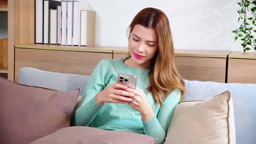 Auburn-haired woman texting on smartphone on couch