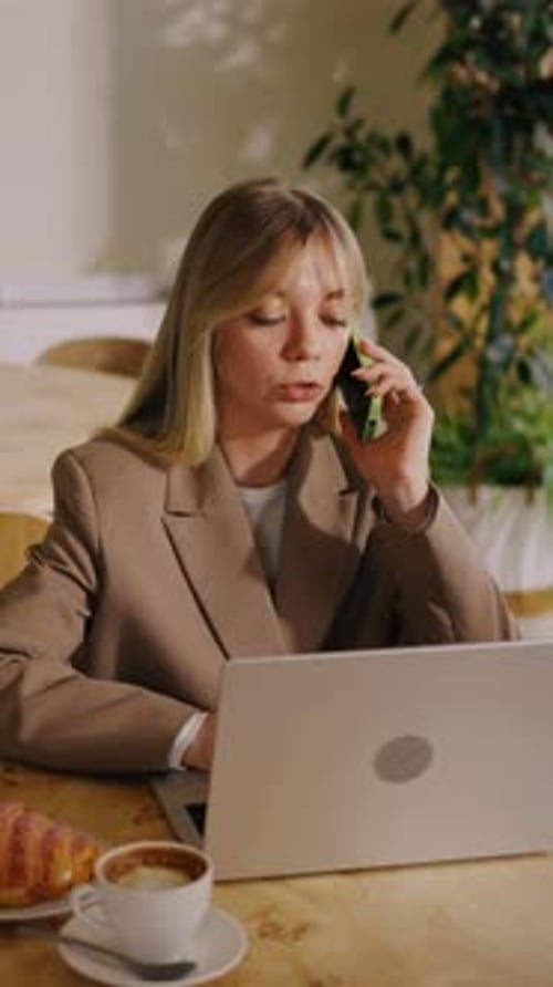 Focused Businesswoman in Beige Blazer Working Remotely at Cozy Cafe Table Multitasking with