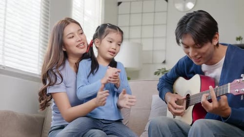 Family sings and plays guitar on sofa indoors