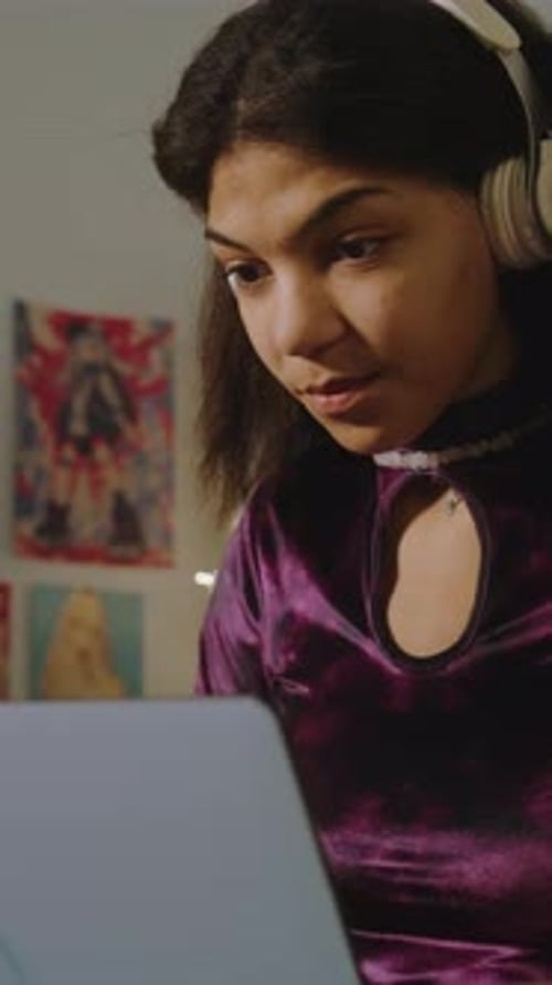 Beautiful Teenager in Headphones Sits on Bed Uses Laptop