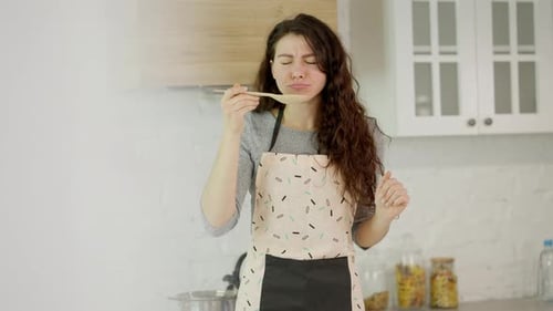 Woman Tastes Food in Kitchen with Spoon