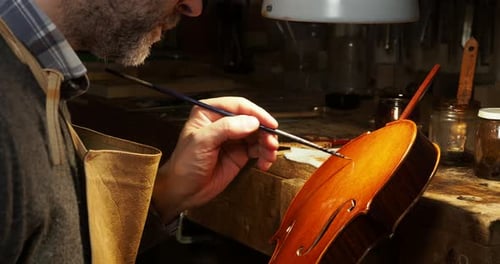 Close up of a violin maker carefully applying varnish on a new handcrafted violin in his workshop