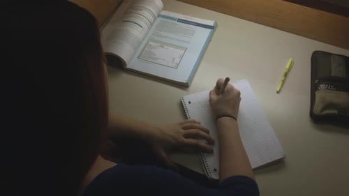 An over the shoulder of a female student making notes in a notebook while studying.