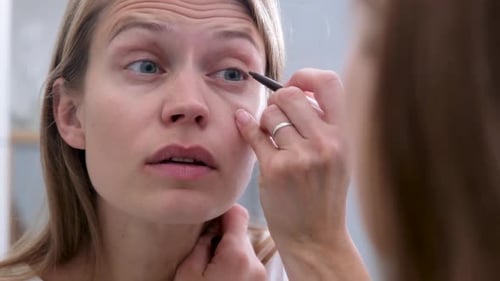Woman Applying Eyeliner in the Bathroom Mirror