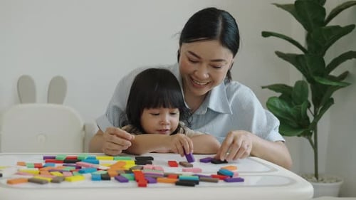 toddler girl and her mother playing colorful wooden block toy or domino game together