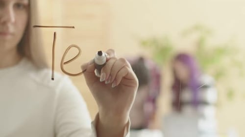 Une femme caucasienne aux cheveux blonds écrit le mot travail d'équipe sur du verre sur fond de groupe
