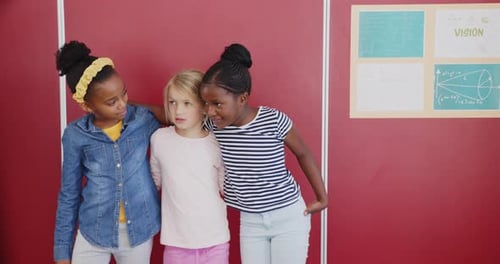 In school, three girls standing together and smiling in classroom