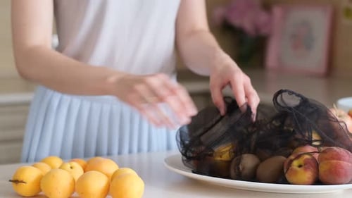 Una mujer apila fruta en la cocina El concepto del vegetarianismo Bolsas ecológicas para almacenar fruta