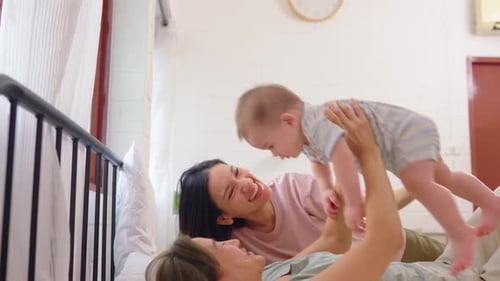 Two Women play with Infant on a Bed