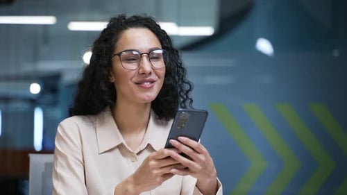 Smiling businesswoman is using mobile phone sitting at a workplace in modern business office. Female