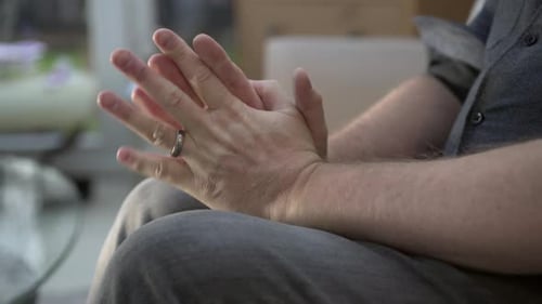 Worried, anxious, stressed male sitting rubbing his hands in desperation.