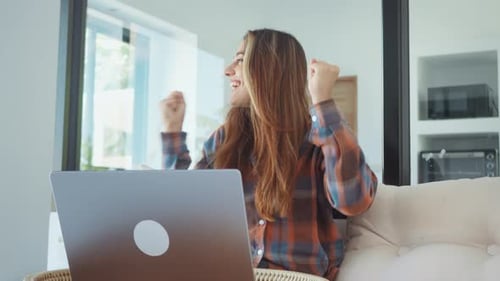Excited Woman Celebrates Success Using Laptop at Home