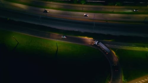 View From Above at Night of Cars Moving on a Highway with Curved Roads and Bright Urban Lights Below