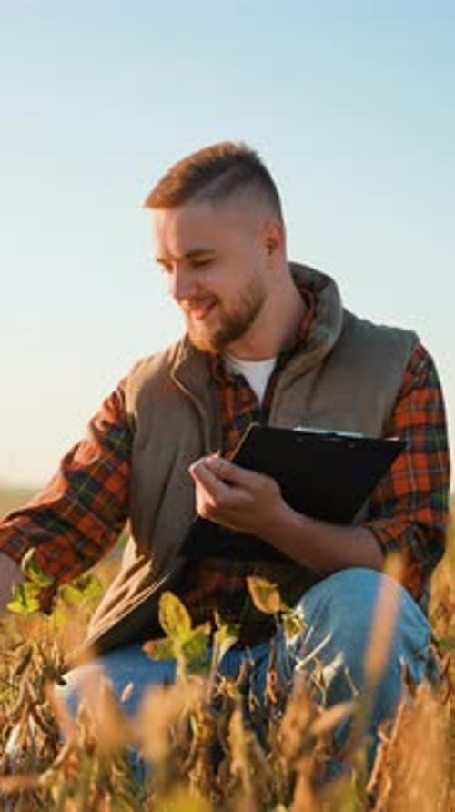 Focused Farmer Inspecting Crops and Taking Notes