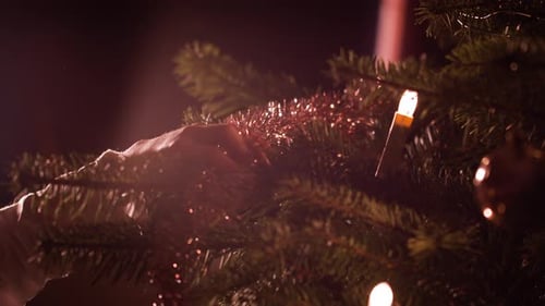 Close up, woman's hands hanging up tinsel decoration onto Christmas tree at home
