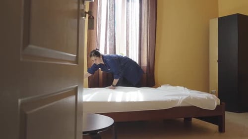 Female Housekeeper Changing Bedding in a Hotel Room