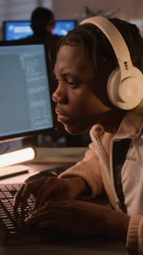 Vertical of Black Software Developer Wearing Headphones Coding in Office