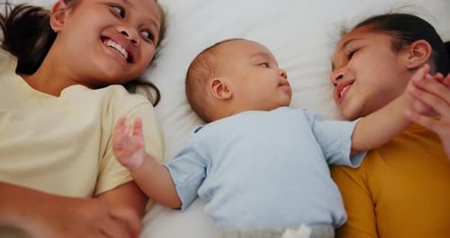 Sisters Laughing with Baby Lying on Bed